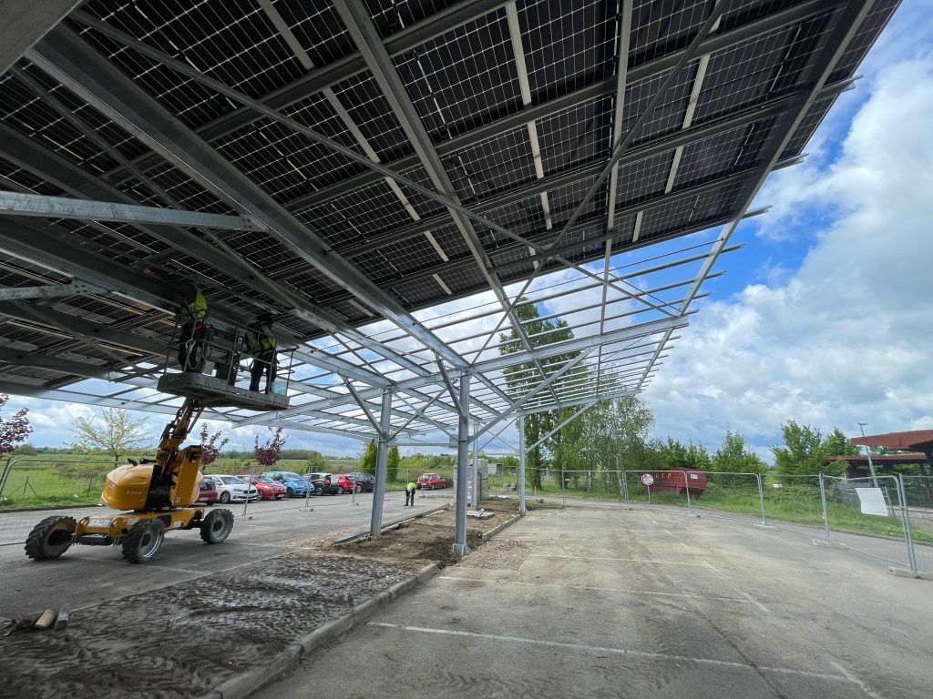 Avancement des travaux d'installation d'une ombrière sur le parking de la halte ferroviaire de St-Marcel-en-Dombes : pose de la quasi-totalité des 270 panneaux photovoltaïques de l'installation et réalisation des travaux électriques à venir